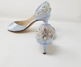 A pair of baby blue satin kitten heels with a peep toe and designed with a crystal design on the front of the shoes and a large crystal design on the back heel of the shoes