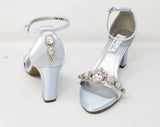 A pair of baby blue block heel shoes with an ankle strap and a crystal design on the front toe strap of the shoes and a crystal design on the heel of the shoes
