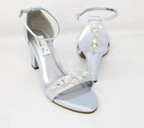A pair of baby blue block heel shoes with an ankle strap and a pearl and crystal design on the front toe strap of the shoes and a pearl and crystal design on the heel of the shoes