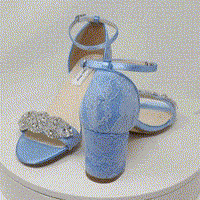 A pair of blue lace covered low block heel shoes with an ankle strap and a crystal design on the front toe strap of the shoes