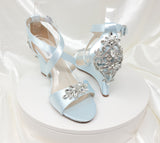 A pair of baby blue wedding shoes with high wedge and straps across the front of the foot designed with a crystal design on the front toe strap and a crystal design on the back heel of the shoes