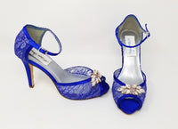 A pair of royal blue high heeled lace shoes with a front platform and a peep toe with a rose gold design on the front of the shoes