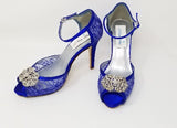 A pair of royal blue high heeled platform lace shoes with an ankle strap and a crystal design on the front of the peep toe shoes