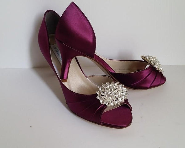 A pair of burgundy satin medium height heel shoes with a peep toe and designed with a crystal design on the front of the shoes