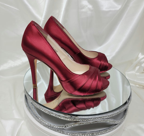 A pair of high heeled burgundy satin shoes with a peep toe and a hidden platform at the front of the shoes 