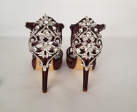 A pair of burgundy high heeled platform lace shoes with an ankle strap and a crystal design on the front of the peep toe shoe and a crystal design on the back heel of the shoes