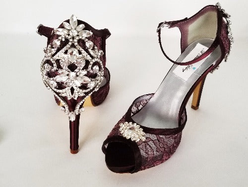 A pair of burgundy high heeled platform lace shoes with an ankle strap and a crystal design on the front of the peep toe shoe and a crystal design on the back heel of the shoes