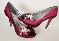 A pair of high heeled burgundy satin shoes with a peep toe and a hidden platform at the front of the shoes and a pearl and crystal design on the front of the shoes
