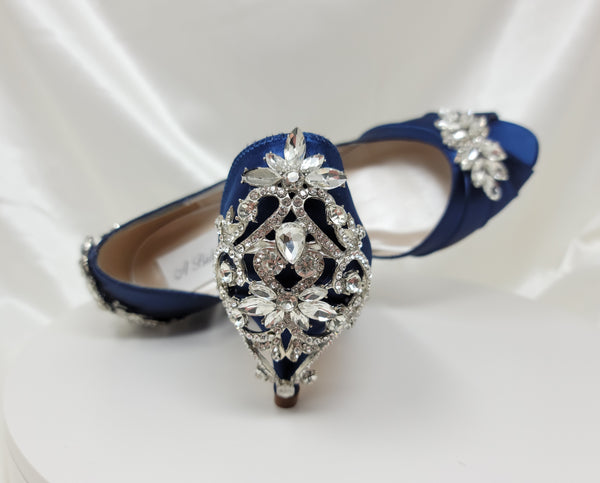 A pair of  bridal shoes in navy blue satin with a kitten heel and a peep toe and a crystal design on the front of the shoes and a crystal design on the back heel of the shoes