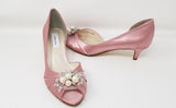 A pair of dusty rose satin kitten heels with a peep toe and designed with a crystal design on the front of the shoes