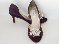 A pair of eggplant purple satin medium height heel bridal shoes with a peep toe and designed with a crystal design on the front of the shoes