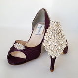 A pair of eggplant purple satin medium height heel bridal shoes with a peep toe and designed with a crystal design on the front of the shoes and a crystal design on the back heel of the shoes