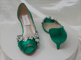 A pair of emerald green satin kitten heel shoes with a peep toe and a crystal vine design on the front and side of the shoes