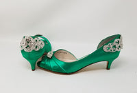 A pair of emerald green satin kitten heels with a peep toe and designed with a crystal design on the front of the shoes and a large crystal design on the back heel of the shoes
