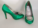 A pair of high heeled emerald green satin shoes with a peep toe and a hidden platform at the front of the shoes and a crystal design on the front of the shoes