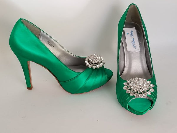 A pair of high heeled emerald green satin shoes with a peep toe and a hidden platform at the front of the shoes and a crystal design on the front of the shoes
