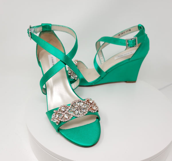 A pair of emerald green wedding shoes with high wedge and straps across the front of the foot designed with a rose gold crystal design on the front toe strap of the shoes