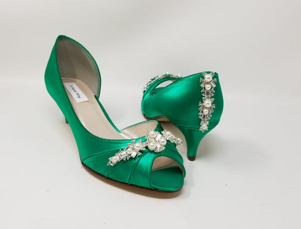 A pair of emerald green satin kitten heels with a peep toe and designed with a pearl and crystal design on the front of the shoes and a pearl and crystal design on the back of the shoes