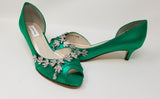 A pair of emerald green satin kitten heel shoes with a peep toe and a crystal vine design on the front and side of the shoes