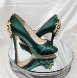 A pair of high heeled hunter green satin shoes with a peep toe and a hidden platform at the front of the shoes and a gold crystal design on the back heel of the shoes