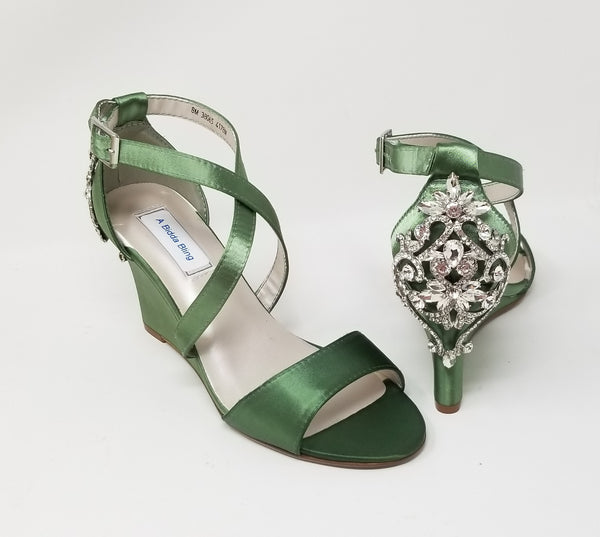 A pair of sage green wedding shoes with high wedge and straps across the front of the foot designed with a crystal design on the back heel of the shoes