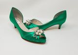 A pair of emerald green satin kitten heels with a peep toe and designed with a pearl and crystal design on the front of the shoes