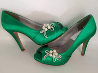 A pair of high heeled emerald green satin shoes with a peep toe and a hidden platform at the front of the shoes and a crystal and pearl design on the front of the shoes