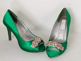 A pair of high heeled emerald green satin shoes with a peep toe and a hidden platform at the front of the shoes and a rose gold crystal design on the front of the shoes
