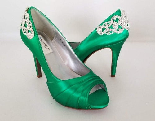 A pair of high heeled emerald green satin shoes with a peep toe and a hidden platform at the front of the shoes and a crystal design on the back heel of the shoes