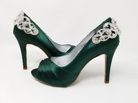 A pair of high heeled hunter green satin shoes with a peep toe and a hidden platform at the front of the shoes and a crystal design on the back heel of the shoes
