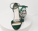 A pair of hunter green block heel shoes with an ankle strap and a crystal design on the front toe strap of the shoes and a crystal design on the heel of the shoes
