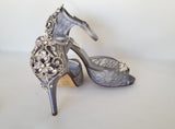 A pair of grey high heeled platform lace shoes with an ankle strap and a crystal design on the front of the peep toe shoe and a crystal design on the back heel of the shoes