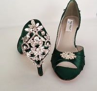 A pair of hunter green satin medium height heel bridal shoes with a peep toe and designed with a crystal design on the front of the shoes and a crystal design on the back heel of the shoes