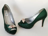 A pair of high heeled hunter green satin shoes with a peep toe and a hidden platform at the front of the shoes a rose gold crystal design on the front of the shoes