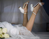 A pair of ivory lace covered low block heel shoes with an ankle strap
