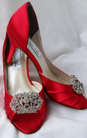 A pair of red satin medium height heel shoes with a peep toe and designed with a crystal design on the front of the shoes 