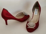 A pair of red satin medium height heel shoes with a peep toe and designed with a crystal design on the front of the shoes