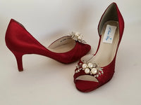 A pair of red satin medium height heel shoes with a peep toe and designed with a crystal and pearl design on the front of the shoes
