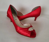 A pair of red satin kitten heel shoes with a peep toe with a small crystal design on the front of the shoes