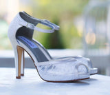 A pair of white lace high heeled shoes with a front hidden platform and an ankle strap with a peep toe