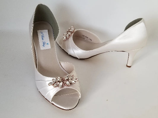 A pair of ivory satin medium height heel bridal shoes with a peep toe and designed with a rose gold crystal design on the front of the shoes
