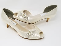 A pair of ivory satin kitten heel shoes with a peep toe and a crystal vine design on the front and side of the shoes