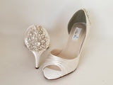 A pair of ivory satin heels with a peep toe and designed with a crystal design on the front of the shoes and a large crystal design on the back heel of the shoes