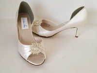 A pair of ivory satin medium height heel bridal shoes with a peep toe and designed with a crystal design on the front of the shoes