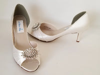 A pair of ivory satin medium height heel bridal shoes with a peep toe and designed with a crystal design on the front of the shoes