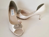 A pair of ivory satin heels with a peep toe and designed with a crystal design on the front of the shoes 