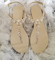 a pair of flat heel ivory bridal sandals with pearls and crystals on the straps of the sandals