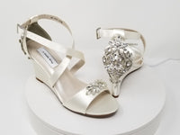 A pair of ivory wedding shoes with high wedge and straps across the front of the foot designed with a crystal design on the front toe strap and a crystal design on the back heel of the shoes