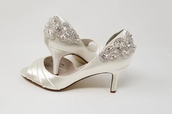 A pair of ivory satin medium height heel shoes with a peep toe and designed with a and crystal design on the front of the shoes and a crystal design on the back heel of the shoes
