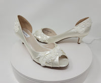 A pair of  ivory satin kitten heels with a peep toe and ivory lace and pearls covering the shoe
